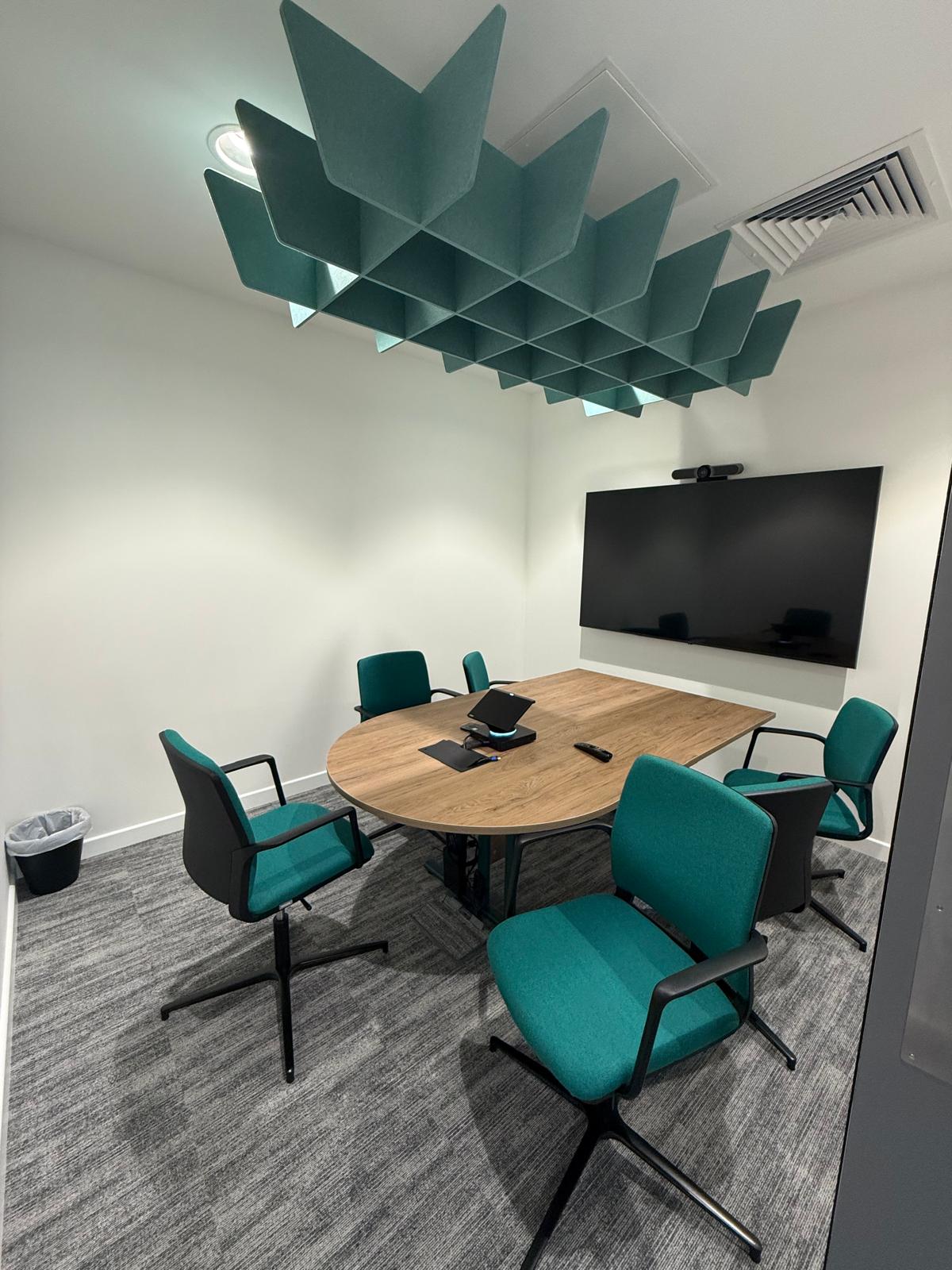 Focus room with a round timber table, green chairs and a geometric acoustic ceiling feature