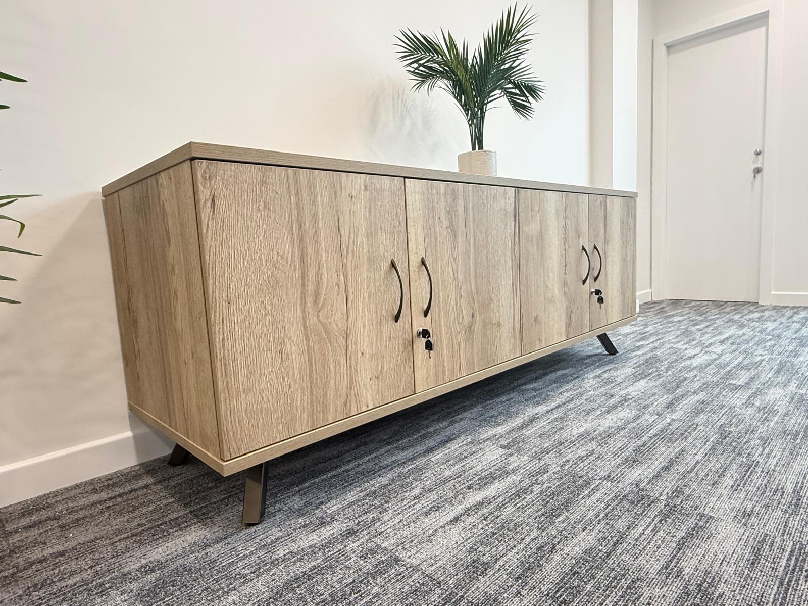 Timber-finish storage credenza with a potted plant in a light office corridor