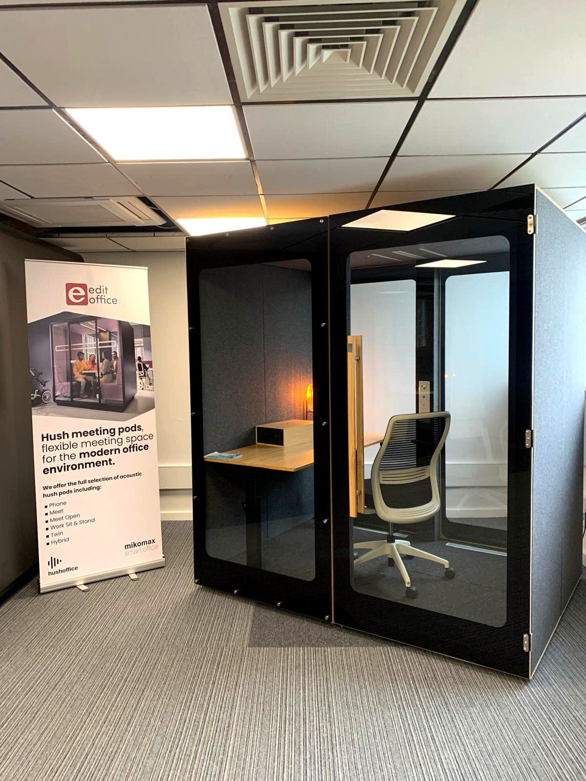 Black acoustic meeting pod with an integrated desk and task chair