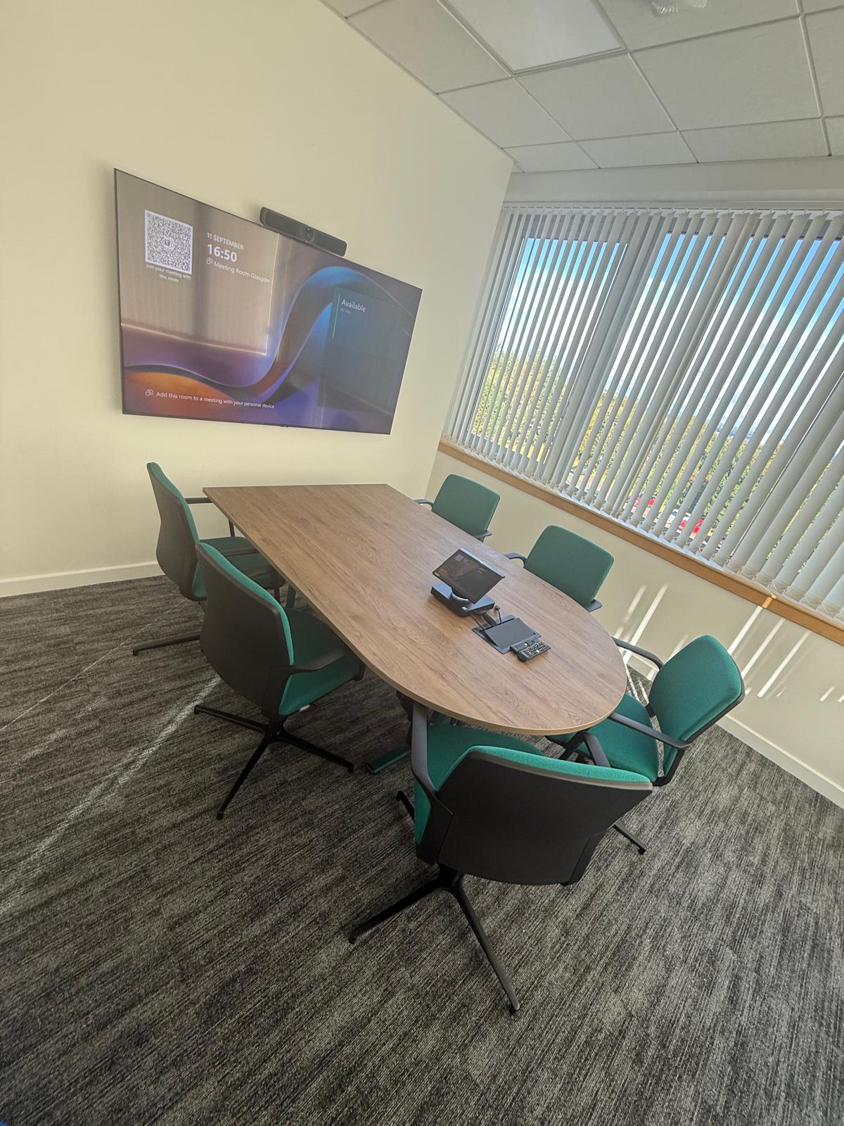 Compact video meeting room with an oval timber table and green meeting chairs