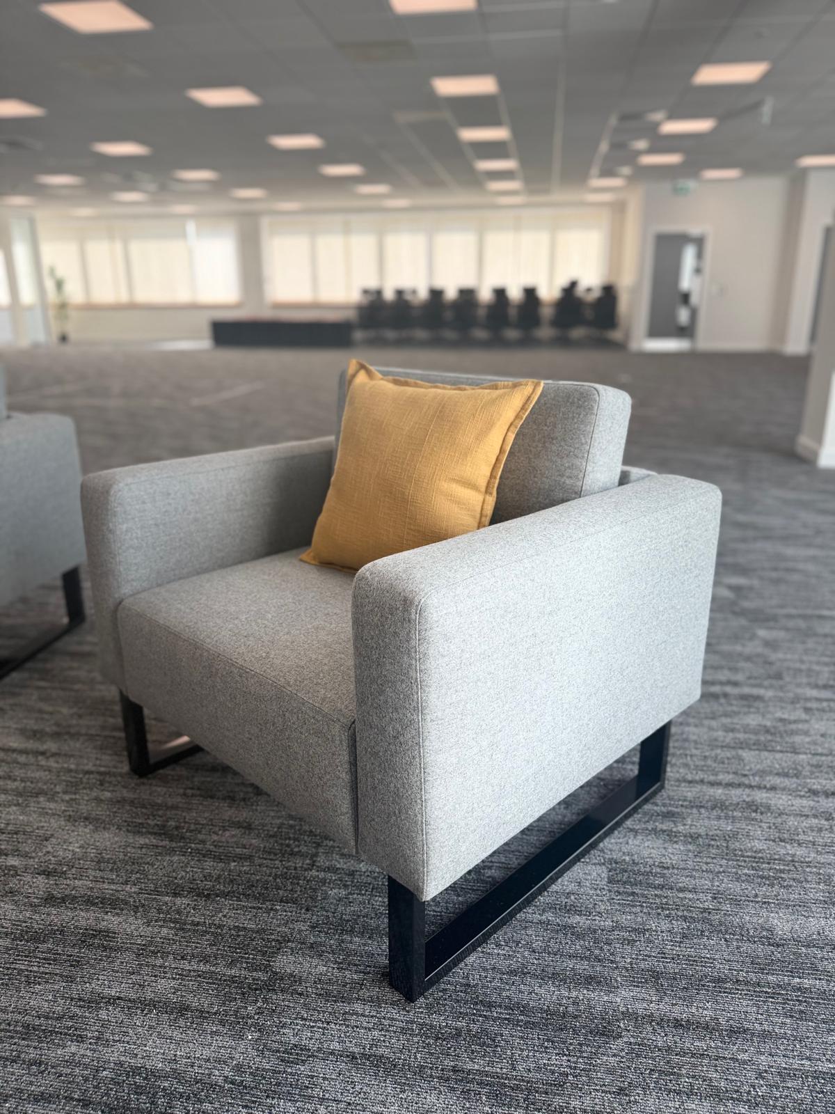 Grey soft-seating armchair with a mustard cushion in the breakout area