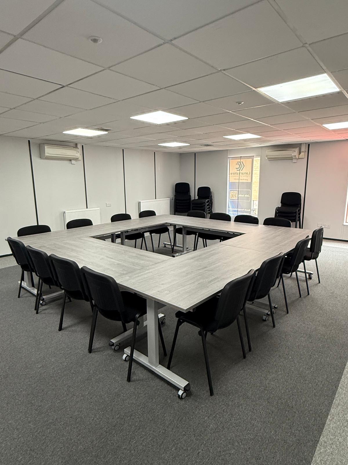 Large hollow-square conference layout with sixteen black chairs around grey tables