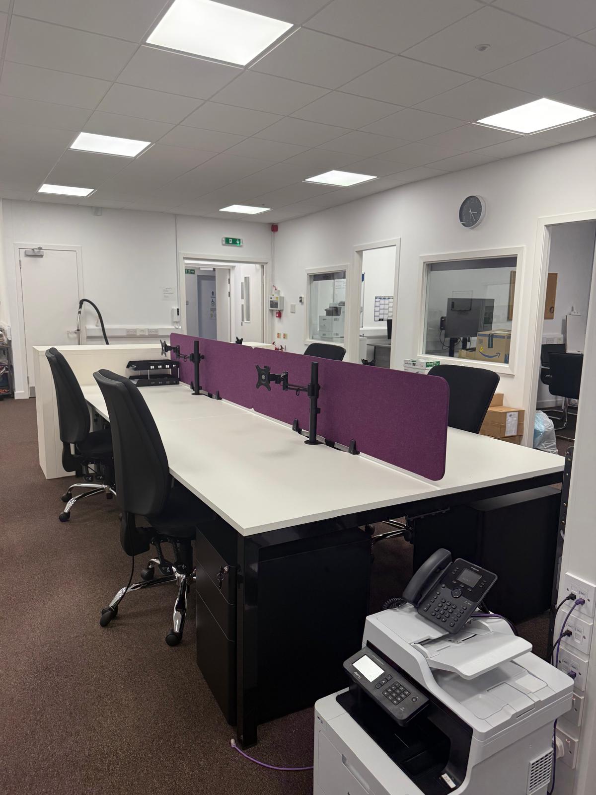 Completed bench desks with purple acoustic screens and task chairs