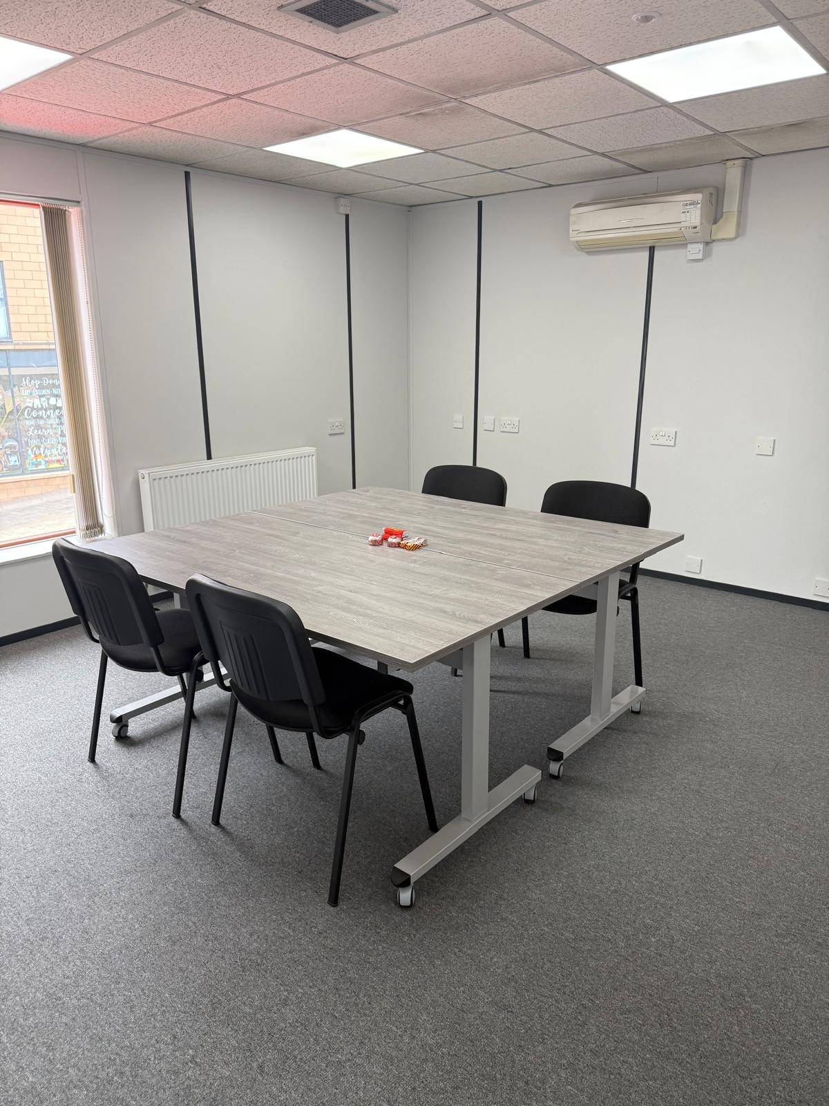 Compact square table arrangement with four black meeting chairs, ready for a workshop session